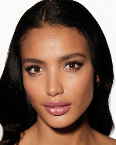 Deep-tone model with brown eyes wearing a moisturising lipstick balm in a sheer nude pink berry shade with a high-shine finish.