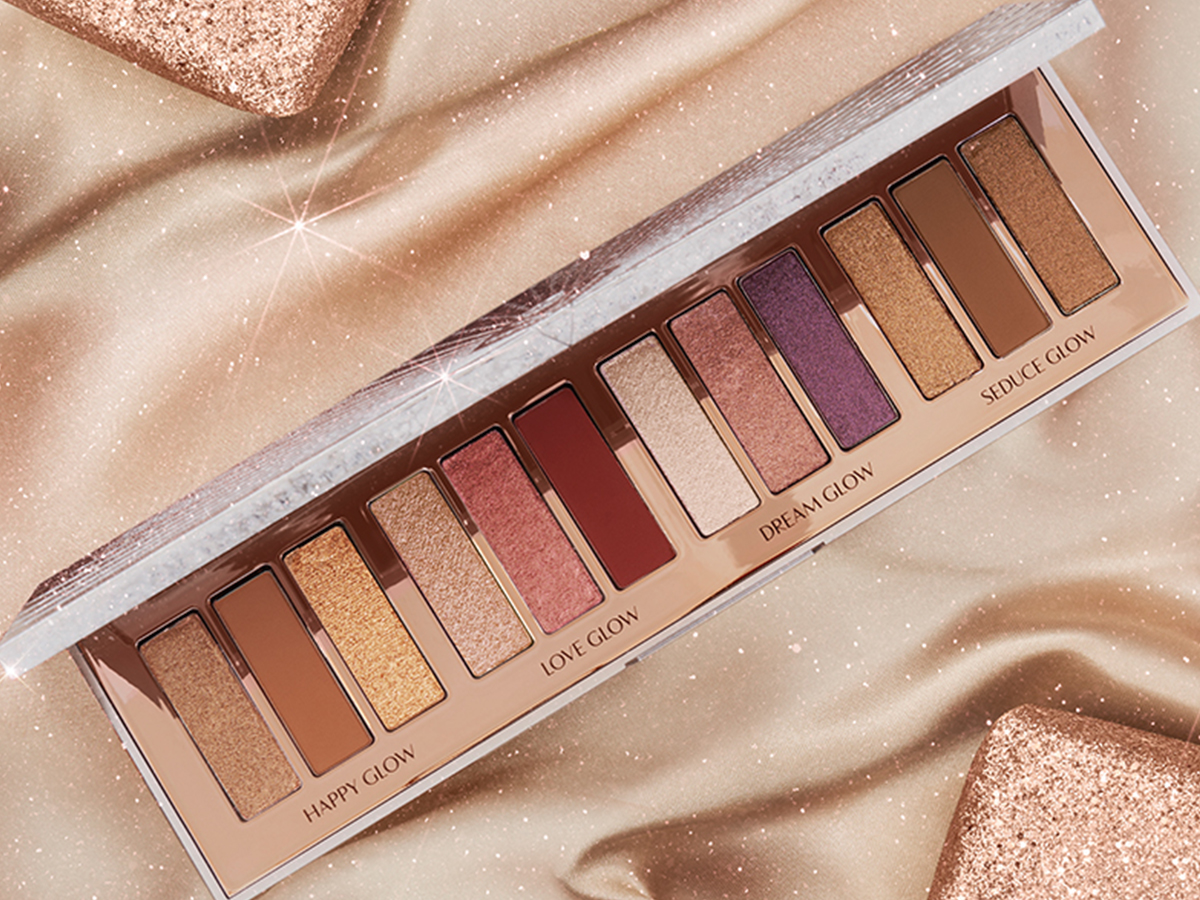 An open, mirrored-lid eyeshadow palette with matte and shimmery orange, brown, pink, purple, red, and gold shades.