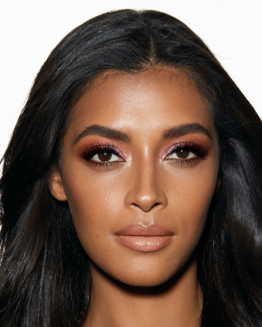 Deep-tone model with brown eyes wearing a nude peach lipstick with shimmery blush pink and smokey brown eyeshadow. 