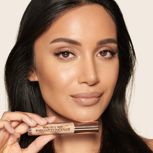 Medium-tone model with brown eyes wearing a radiant, concealer that brightens, covers blemishes, and makes her skin look fresh along with nude lip gloss and subtle eye makeup.
