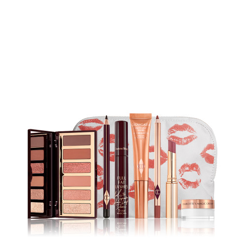 An open, mirrored-lid eyeshadow palette in nude brown and peach shades, an open eyeliner pencil in black, mascara, highlighter wand in peach packaging, lip liner pencil in redwood, lipstick lip balm in sheer red, and mini face cream in a glass pot, with all products displayed in front of a white-coloure makeup pouch. 