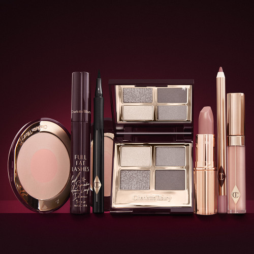 An open, mirrored-lid eyeshadow palette in matte and shimmery silver, grey, and beige shades, an open black eyeliner pen, a mascara in a dark-crimson colour scheme, a nude-pink lipstick with a matching lip liner pencil, nude pink lip gloss, and an open two-tone blush in muted rose-gold and pink. 