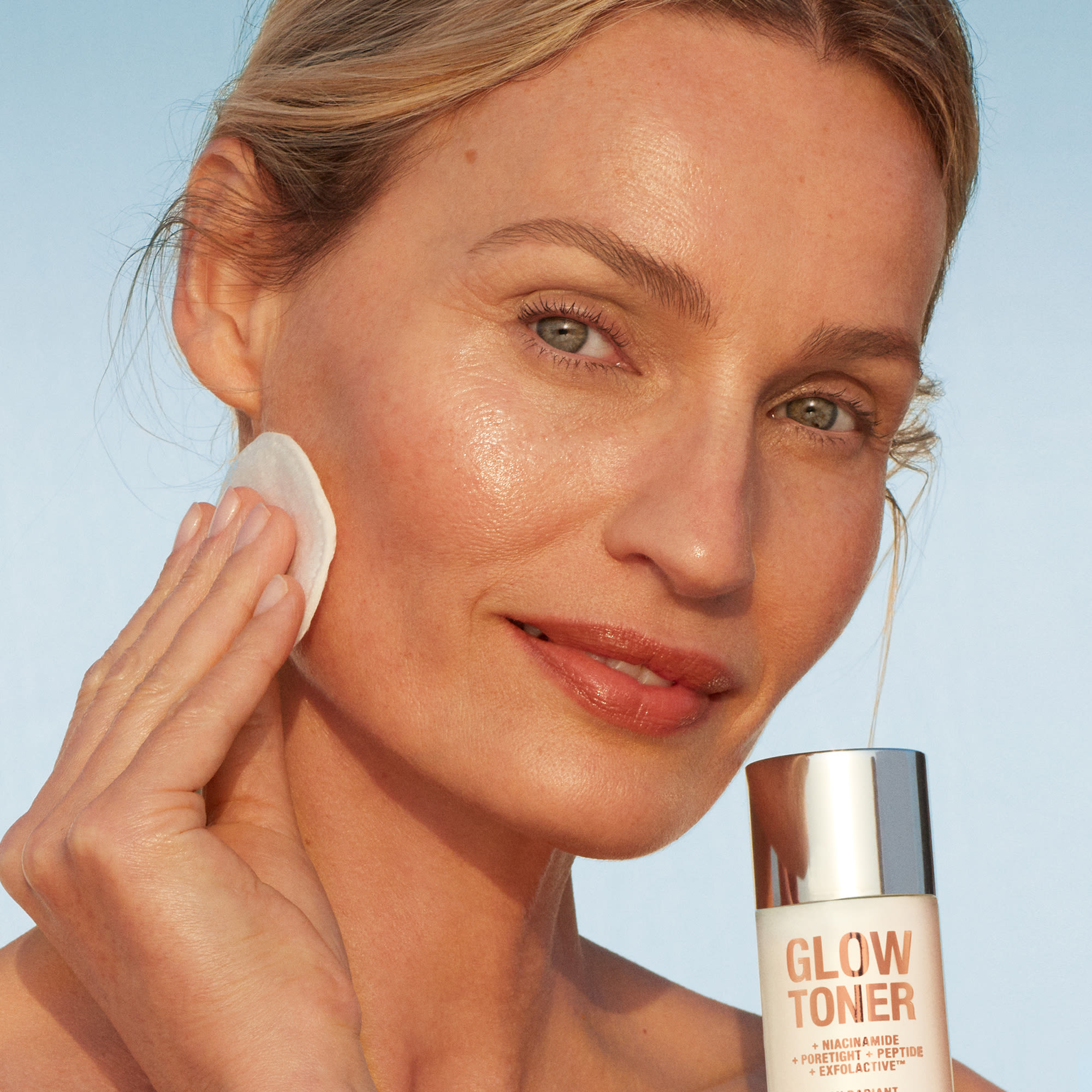 Fair-tone blonde model with glowy, luminous skin, applying glowy toner with a cotton pad.