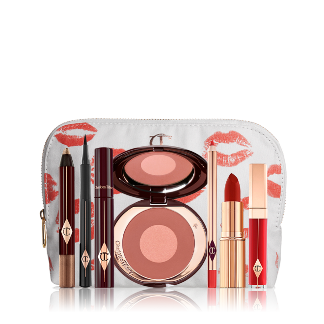 A white-coloured makeup pouch with an open two-tone blush in cool-toned terracotta and warm pink with a mascara, eyeliner pen, an open lipstick in bold red, lip liner pencil in blood-red, and a lip gloss in bright red. 