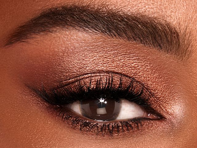 Single-eye close-up of a deep-tone model with brown eyes wearing shimmery topaz and brown eye shadow.