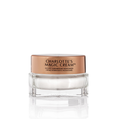 A closed, travel-sized pearly-white face cream in a glass jar with a gold-coloured lid with text on it, 'Charlotte's magic cream'.