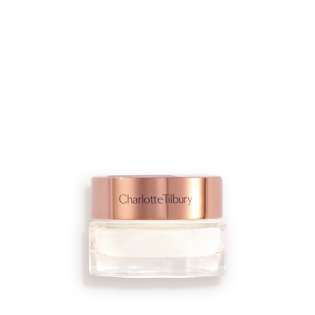 A closed, travel-sized pearly-white face cream in a glass jar with a gold-coloured lid with text on it, 'Charlotte's magic cream'.