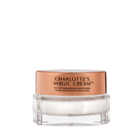 A closed, travel-sized pearly-white face cream in a glass jar with a gold-coloured lid with text on it, 'Charlotte's magic cream'.