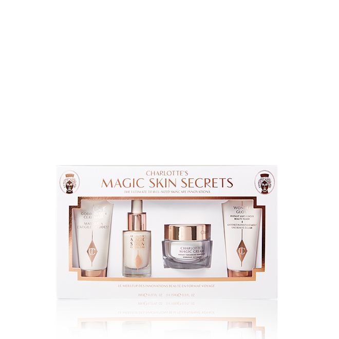 Charlotte's Magic Skin Secrets packed Pearly-white face cream in a glass jar with gold-coloured lid, luminous face serum in a glass bottle with a white and gold-coloured dropper lid, and a clay mask and glowy primer in white-coloured bottles with gold-coloured lids, all packed in a white-coloured box.