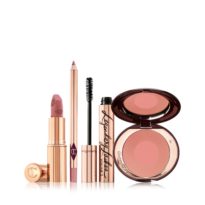An open matte lipstick in nude pink with a nude-pink lip liner pencil, black mascara in gold packaging, and two-tone blush in a warm pink shade. 