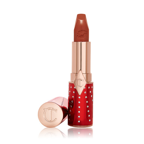 An open tube of lipstick in sparkly red and gold packaging in a matte brick red shade,