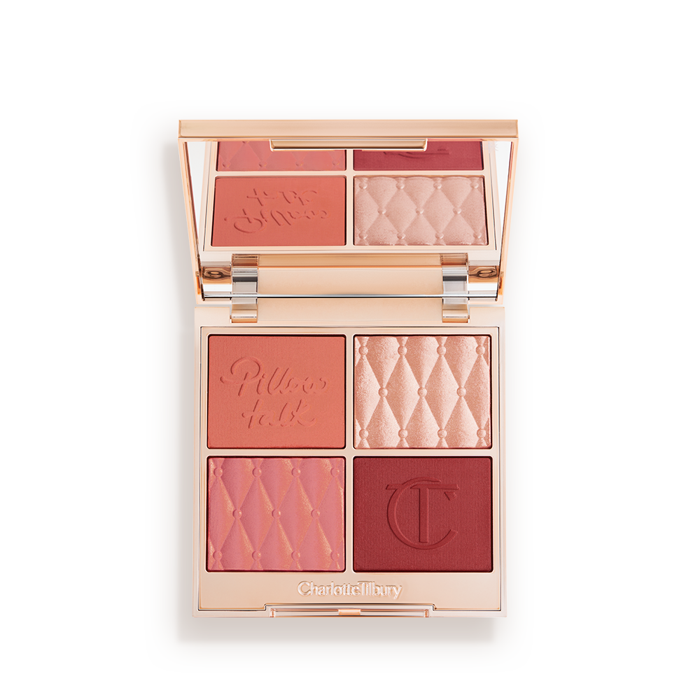 An open, face palette with matte and shimmery eyeshadows, blushes and highlighters in shades of pink, red. and gold with a mirrored lid.
