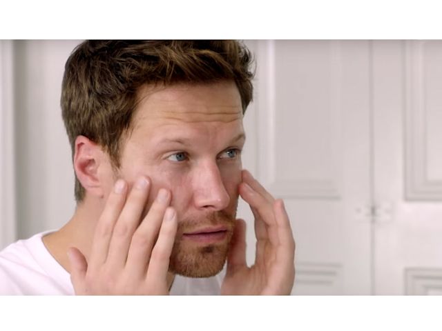 A light-tone, brunette male model patting a face cream into the skin. 