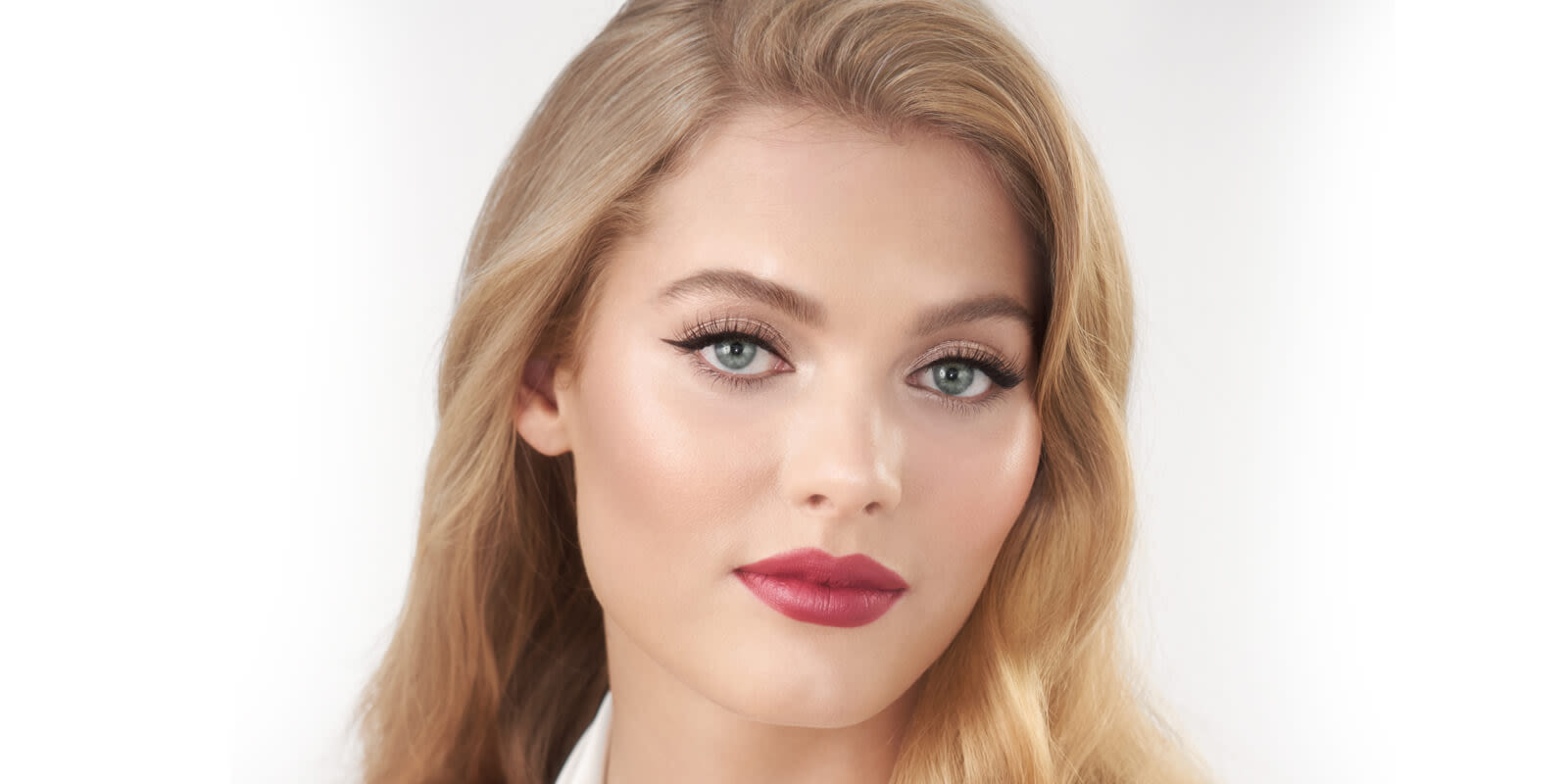 A fair-tone model with blue eyes wearing a matte lipstick in a blushed berry-rose colour. 