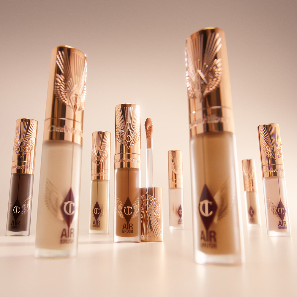 Charlotte Tilbury Airbrush Flawless concealers in various shades arranged in a soft-focus display, featuring rose-gold caps and one open tube with a doe-foot applicator.