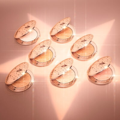 Collection of open, powder highlighter compacts in shades of gold, brown, pink, and silver in sleek, golden-coloured lids.