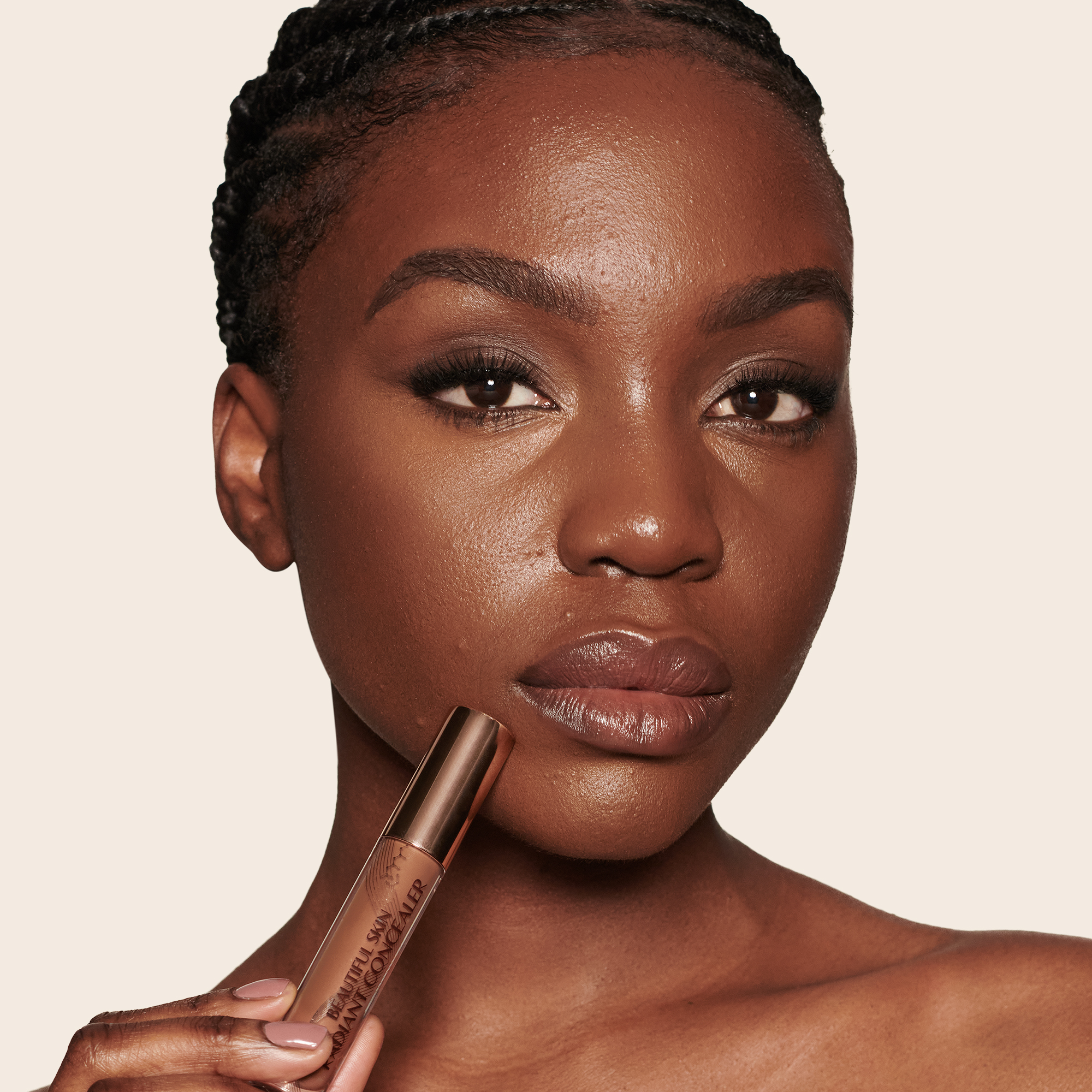Deep-tone model with brown eyes wearing a radiant, concealer that brightens, covers blemishes, and makes her skin look fresh along with nude lip gloss and subtle eye makeup.