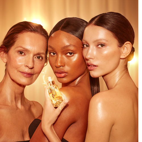 Light, tan, and deep-tone models with glowy, luminous, glass skin, holding up a light-gold-coloured facial oil in a glass bottle with a gold and white-coloured dropper lid.