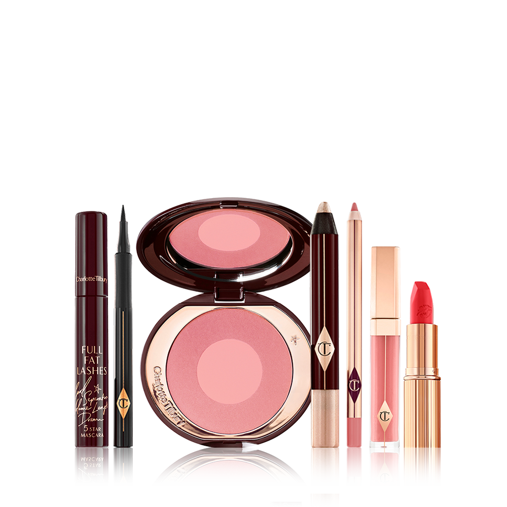 A 7-piece makeup kit containing a mascara, a black eyeliner pen, a pink two-tone blush, cream eyeshadow stick, nude pink lip liner pencil, nude pink lip gloss, and a bright orange-red lipstick. 