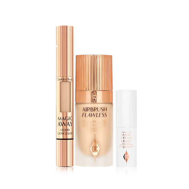 Charlotte's Magic Airbrush Complexion Kit displayed Creamy liquid concealer in a gold-coloured tube with a soft sponge applicator end, foundation in a frosted glass bottle with a gold-coloured lid, and pearly-white face cream in a glass jar with a gold coloured lid.