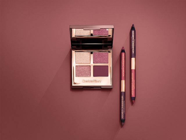 An open, mirrored-lid eyeshadow palette in purple shades with two identical double-sided eyeliner pens in maroon and plum. 