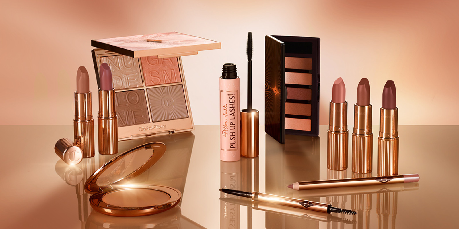 A collection of five open lipsticks in nude shades of pink, brown, and red, black mascara in a pink-coloured tube with a gold-coloured lid, face palette with glowy blush, highlighter, eyeshadow, and contour powders, bronzer compact, lip liner in a taupe shade, and double-ended eyebrow pencil.