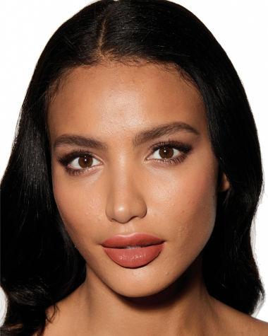 Deep-tone model with brown eyes wearing a moisturising lipstick balm in a peachy-nude shade with a high-shine finish.