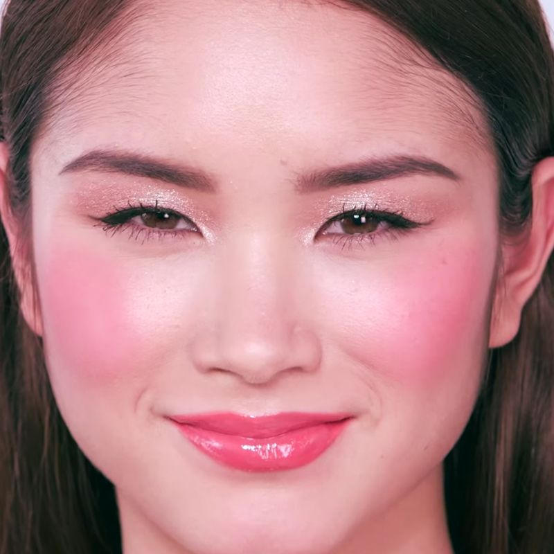 Close-up of a fair-tone brunette model wearing shimmery rose-gold and champagne eye makeup with bright pink blush and glossy strawberry-red lips. 