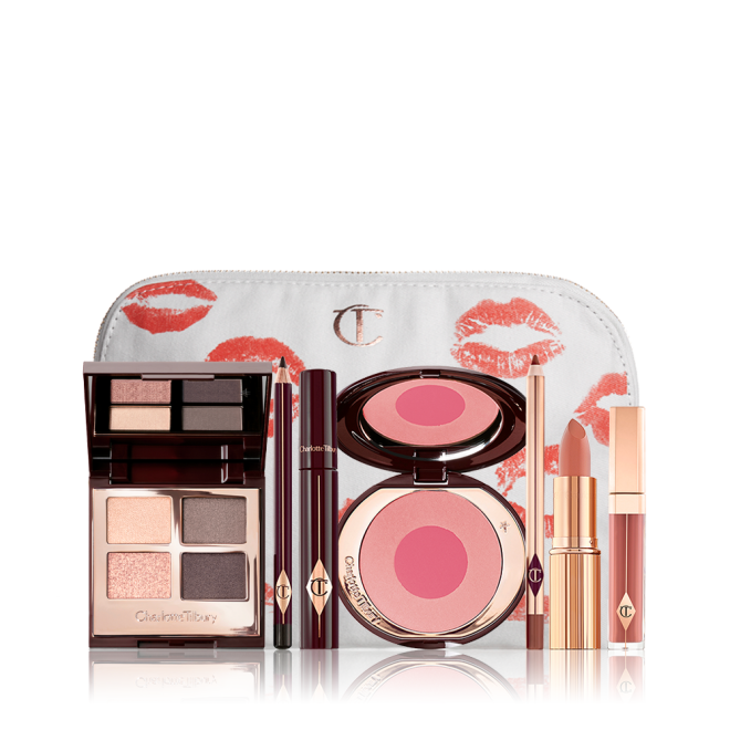 A makeup bag with 7 makeup products, an open two-tone blush in cool-toned pink and fuchsia with a mascara, eyeliner pencil, quad eyeshadow palette with shimmery and matte grey and golden shades, an open lipstick in nude red, lip liner pencil in taupe-brown, and a lip gloss in warm brown-peach. 