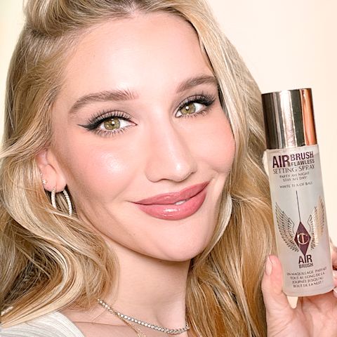 Sofia Tilbury wearing flawless, glowy, soft pink makeup with black eyeliner and holding a large bottle of scented setting spray.