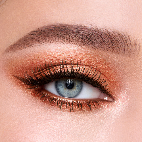 Single-eye close-up of a fair-tone model with blue eyes wearing shimmery peach and smokey copper eyeshadow with black eyeliner.