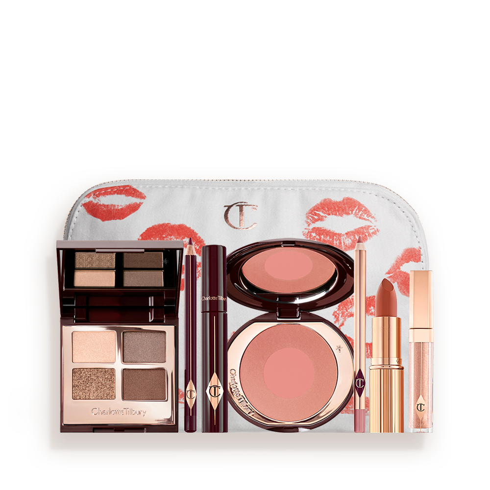An open, mirrored-lid eyeshadow palette in matte and shimmery gold, brown, and beige shades, an open black eyeliner pencil, a mascara in a dark-crimson colour scheme, a golden-peach lipstick with a nude pink lip liner pencil, nude-peach lip gloss, and an open two-tone blush in muted brown-pink. 