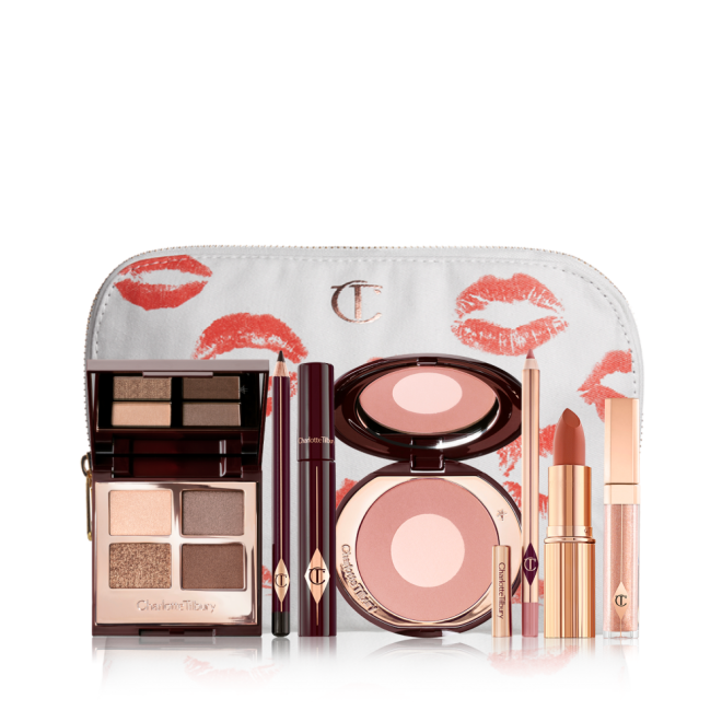 An open, mirrored-lid eyeshadow palette in matte and shimmery gold, brown, and beige shades, an open black eyeliner pencil, a mascara in a dark-crimson colour scheme, a golden-peach lipstick with a nude pink lip liner pencil, nude-peach lip gloss, and an open two-tone blush in muted brown-pink. 