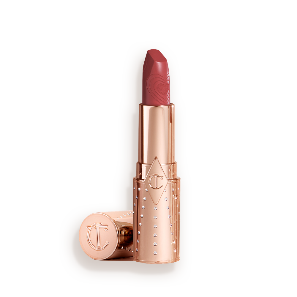 Un labial abierto de acabado en un tono rosa con tubo dorado con la tapa a un lado.