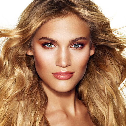 A fair-tone, blonde model wearing a rose-gold, glowy makeup ideal for a summer wedding. 