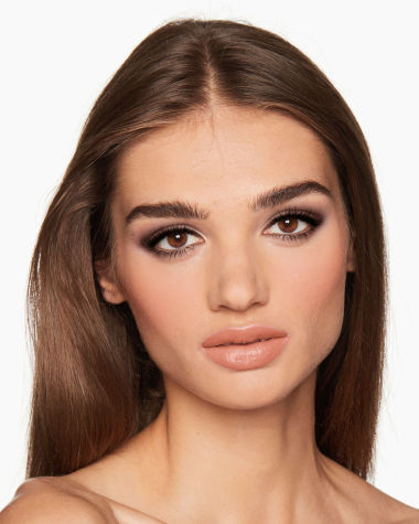 A medium-tone model with brown eyes wearing smokey brown eye makeup with muted pink blush with glossy soft-brown lips