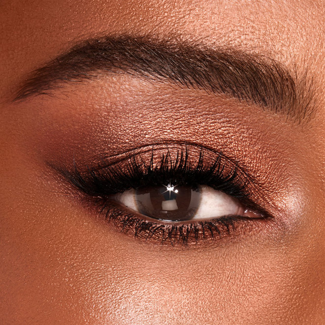 Single-eye close-up of a deep-tone model with brown eyes wearing shimmery brown and gold eye makeup. 