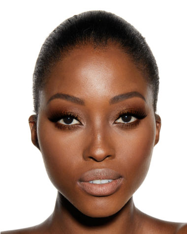 A deep-tone model with brown eyes wearing shimmery gold and bronze eye makeup with black eyeliner and nude peach lipstick. 