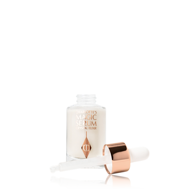 Charlotte's Crystal Elixir travel size open An open, travel-size, pearlescent serum in a glass bottle with its white rose gold coloured dropper lid next to it.