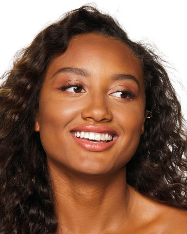 Deep-tone model with brown eyes wearing a universally flattering, peachy-nude lipstick with a satin-finish.