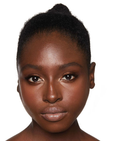 Deep-tone model with brown eyes wearing a pale pink matte lipstick with shimmery terracotta eyeshadow, rosy peach blush, and dark glowy bronzer. 