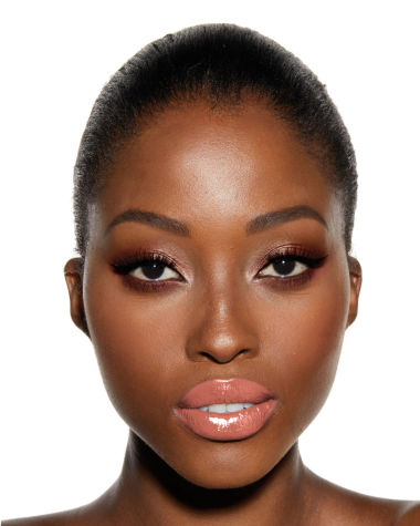 A deep-tone model with brown eyes wearing smokey brown and gold eye makeup with warm pink blush and glossy nude-pink lips