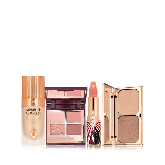 Foundation in a glass bottle with gold-coloured lid, open mirrored-lid quad eyeshadow palette with an open, nude peach lipstick in a funky tube with a panther on it, and duo contour palette with a mirrored-lid. 