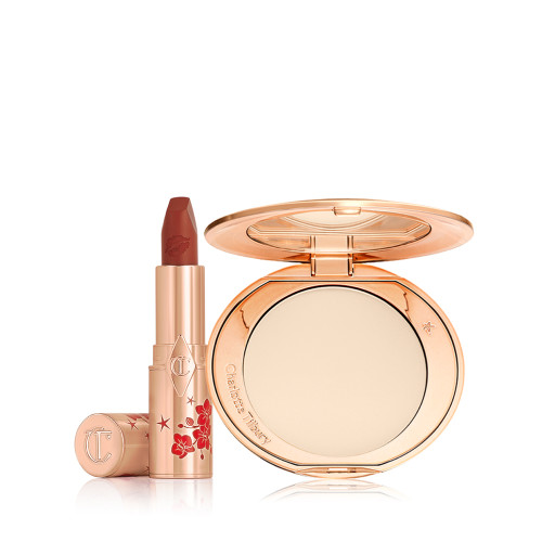 A matte burnt-orange red lipstick in gold-coloured packaging with cherry blossoms illustrated on the tube for the Lunar New Year, along with its lid next to it and an open, pressed powder compact for fair skin tones with a mirrored lid, in gold-coloured packaging with red-coloured cherry blossoms on the lid.