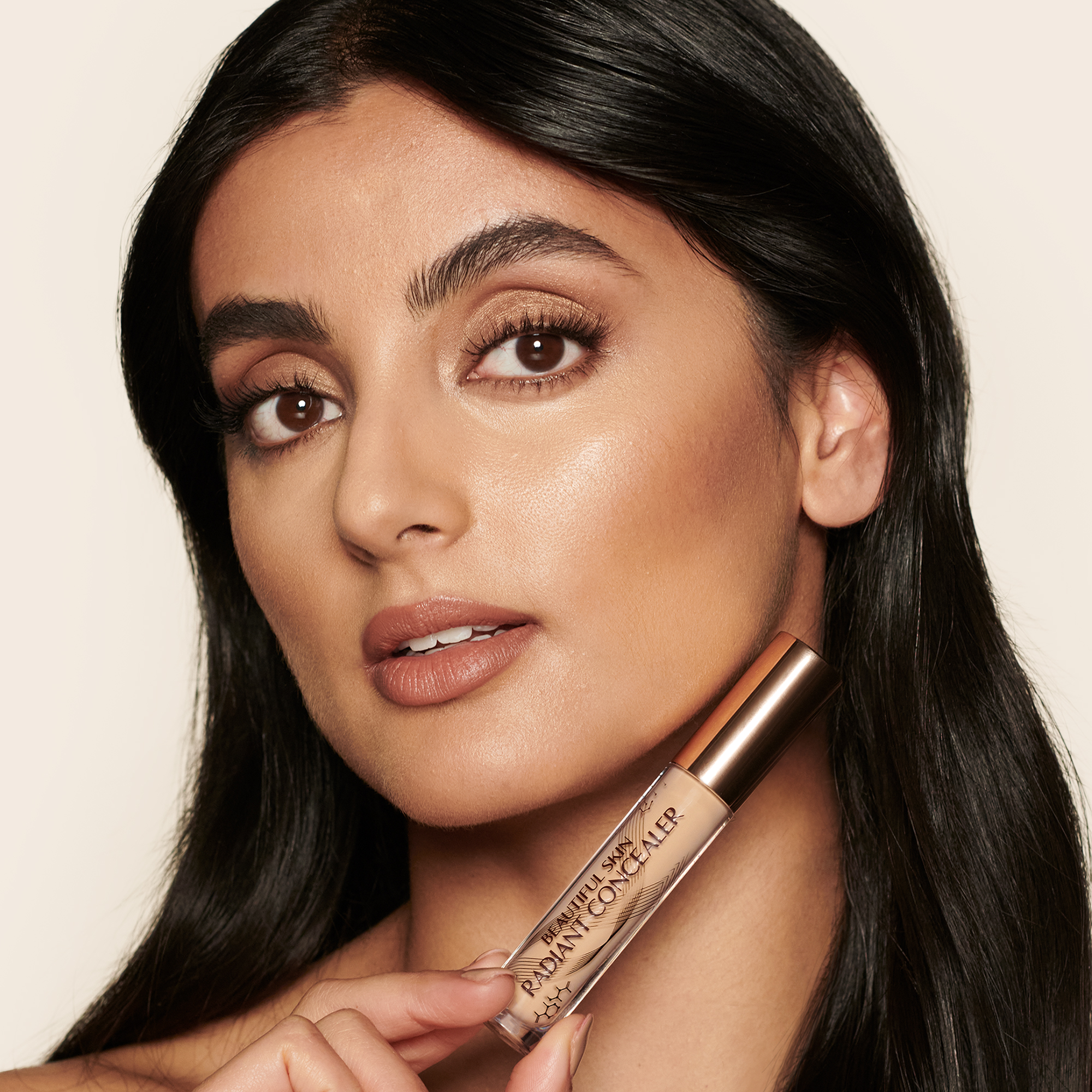 Medium-tone model with brown eyes wearing a radiant, concealer that brightens, covers blemishes, and makes her skin look fresh along with nude lip gloss and subtle eye makeup.