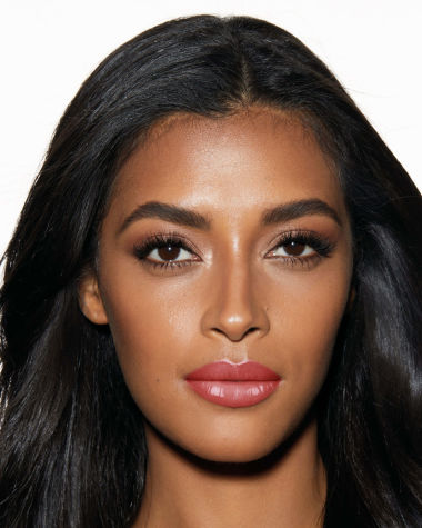 Deep-tone with brown eyes wearing shimmery cream-coloured eye makeup with a high-shine rosy-pink tinted lip oil. 