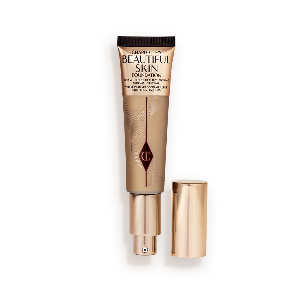 An open foundation wand in gold packaging with a pump dispenser and a medium-brown-coloured body to show the shade of the foundation inside. 