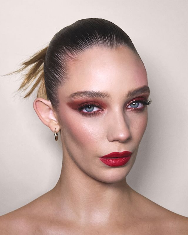 Close-up of a fair-tone model with blue eyes wearing bold red matte lipstick with berry rose and brown dramatic eye makeup with berry rose blush.