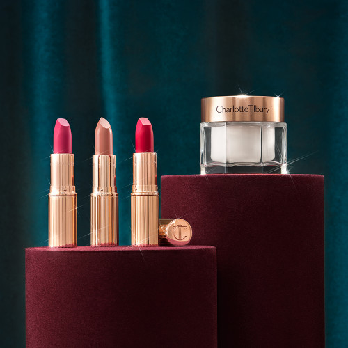 Banner with a pearly-white face cream in a glass jar with a gold-coloured lid, and three open lipsticks, two with a matte finish in magenta and raspberry pink and a satin finish one in a soft rosy peach shade.