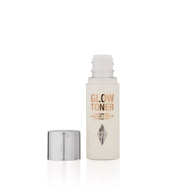An open, travel-size, clear bottle filled with luminous, cream-coloured watery toner with its silver-coloured lid next to it.
